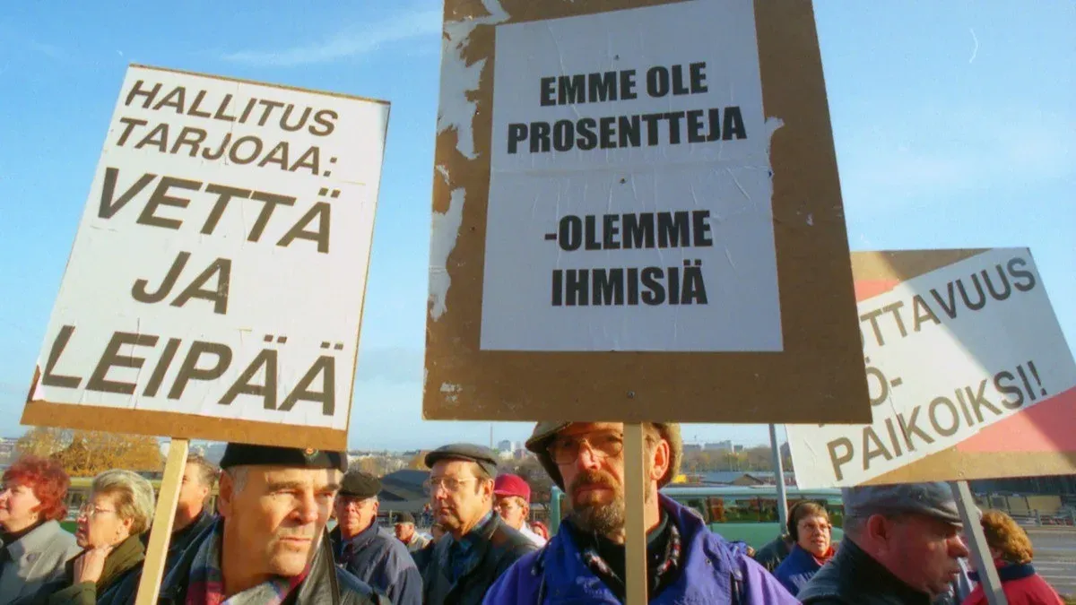 Demonstrators in Helsinki holding placards reading “Hallitus tarjoaa: vettä ja leipää” (The government offers: water and bread) and “Emme ole prosentteja, olemme ihmisiä” (We are not percentages, we are people).