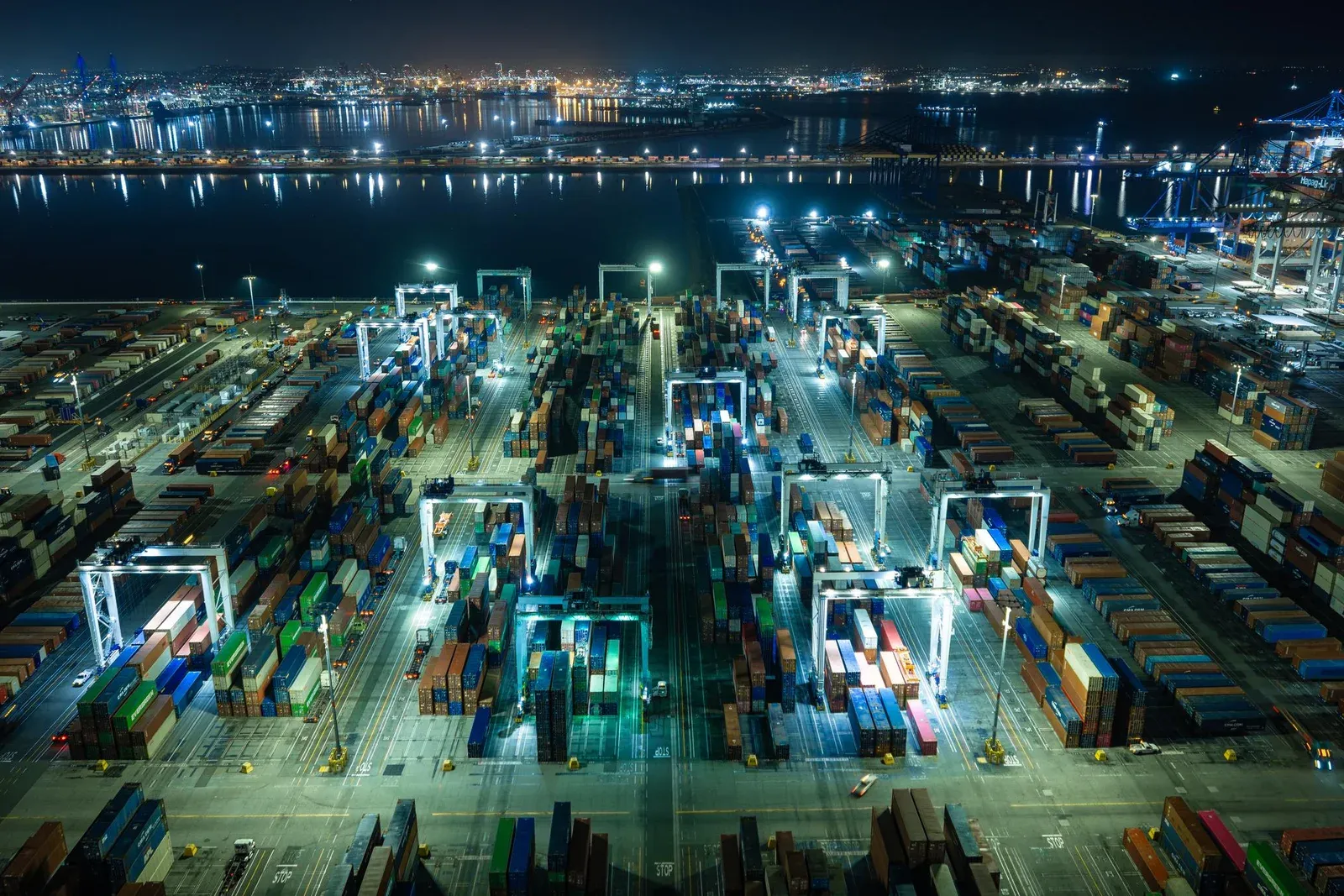 Aerial night view of an automated container port, lit cranes over rows of containers.
