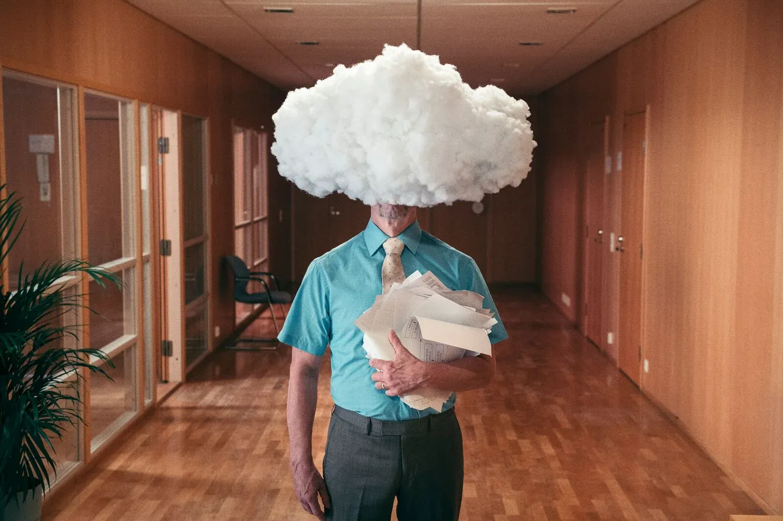 A man in an office corridor holding papers, his head hidden by a white cloud.