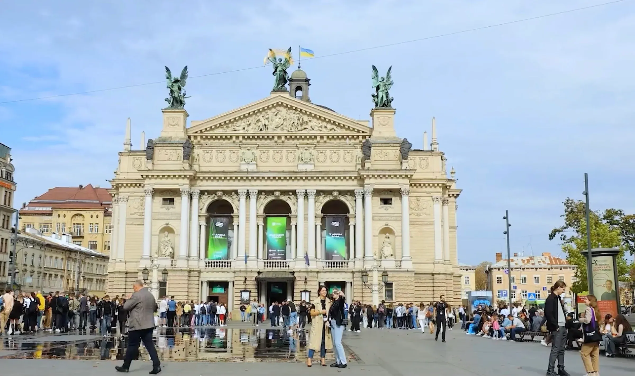 The Lviv Opera with IT Arena 2024 banners between its columns, people gathering in the square outside.