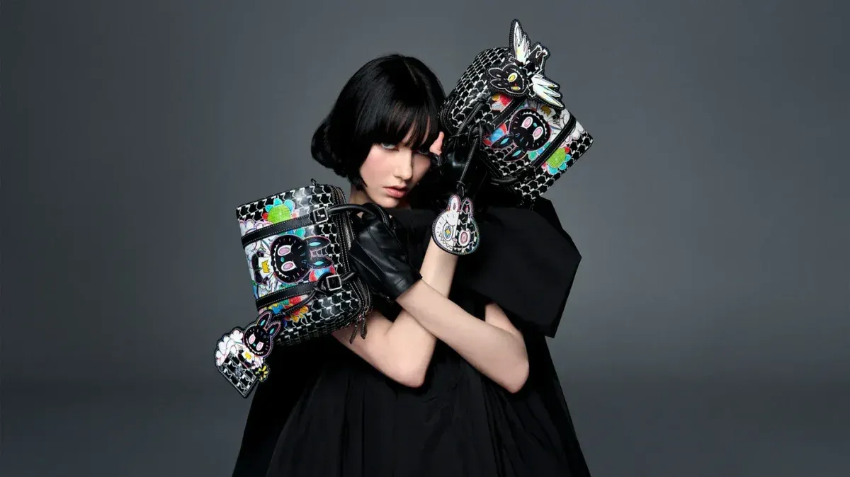Fashion photo: a model in black holding two patterned handbags with cartoon charms.