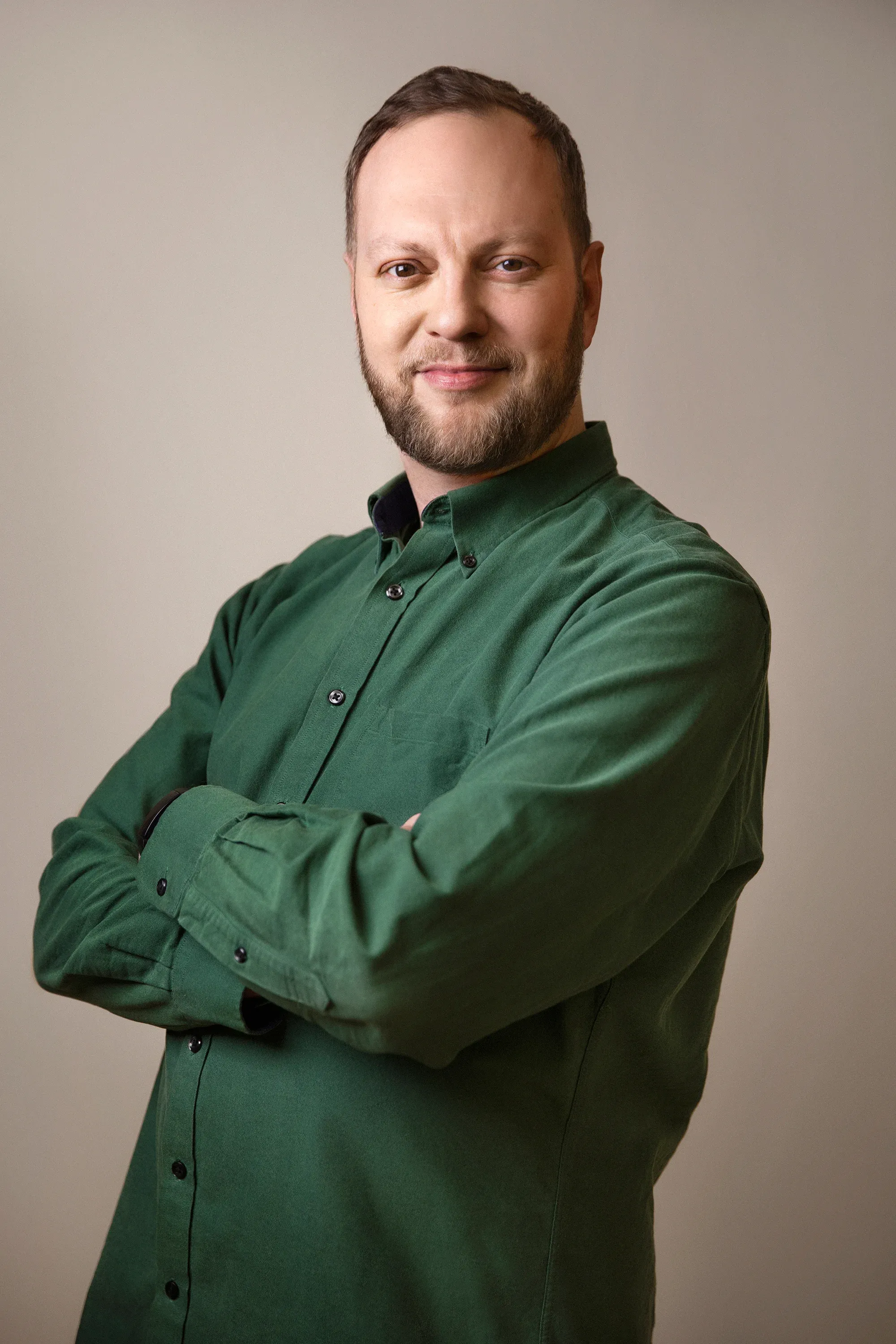 Erik Mashkilleyson in a green shirt, arms crossed, against a warm grey wall.