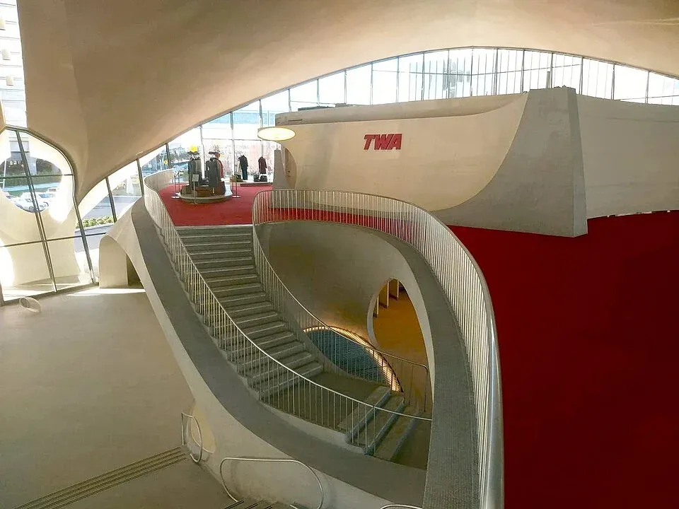 Kaartuvat valkoiset portaat ja kulkusillat TWA Flight Centerissä, punainen matto ja TWA-kyltti.