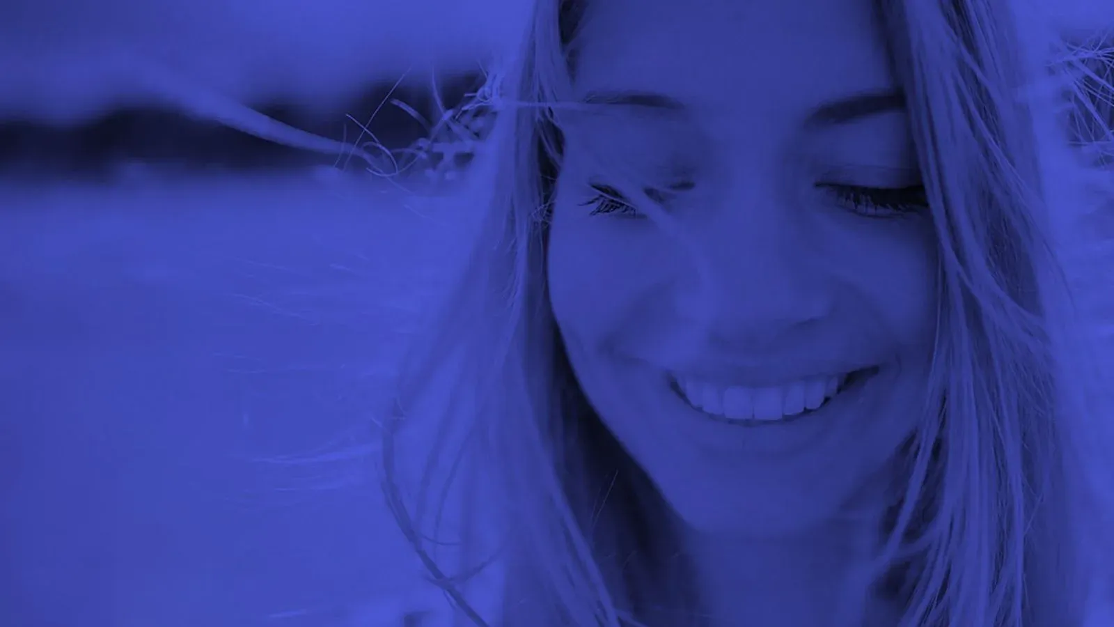 A woman smiling with closed eyes, her hair lit by the sun, in LounaLab's ultramarine duotone.