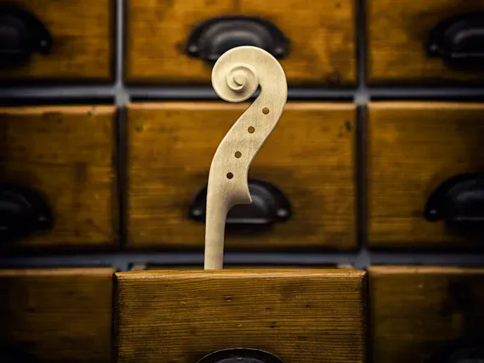 A carved violin scroll in front of old wooden drawers in a luthier’s workshop.