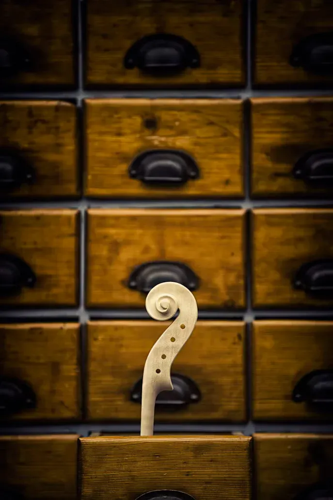 A carved violin scroll in front of old wooden drawers in a workshop.