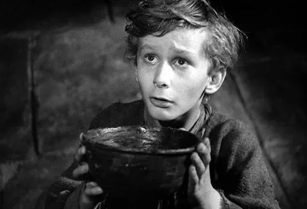 Black-and-white film still: a boy holding up an empty bowl.