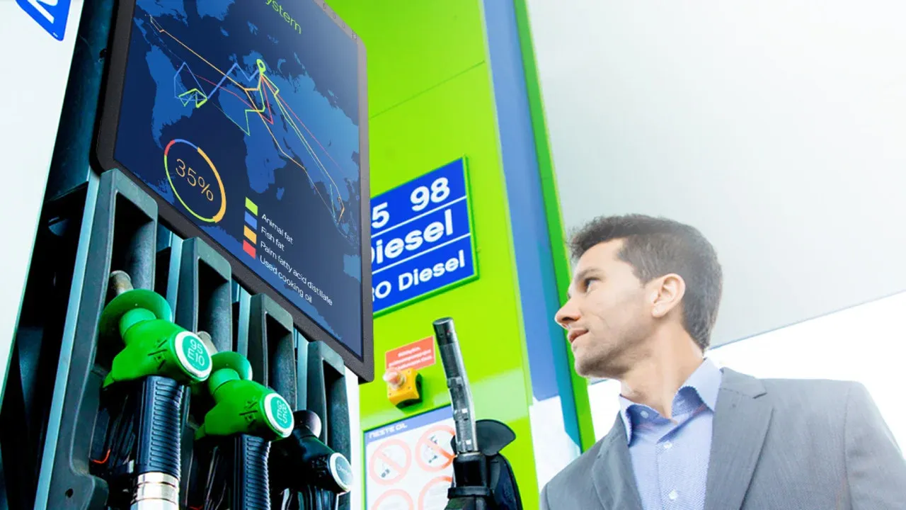Erik in front of a Neste pump with a renewable diesel price display.