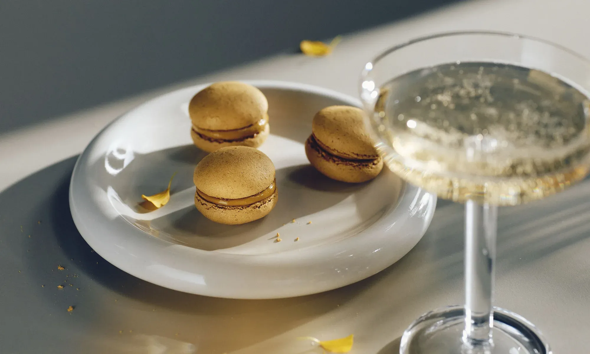 Kolme macaron-leivosta lautasella kuohuviinilasin vieressä.